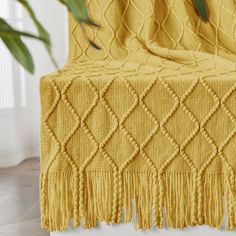 a yellow blanket with tassels on it sitting next to a potted plant