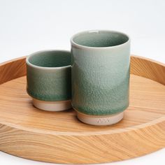 two green cups sitting on top of a wooden tray