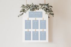 a wedding seating chart hanging on a white wall with eucalyptus leaves and gold clothes pins