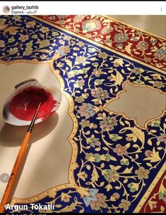 a bowl of red liquid sitting on top of a table next to a paintbrush