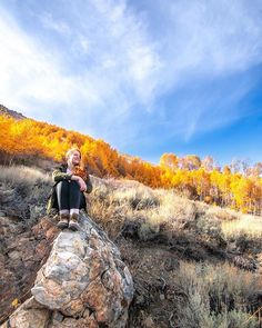 a woman sitting on top of a rock in the middle of an autumn forest with yellow trees