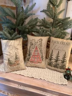 three christmas pillows sitting on top of a table next to a potted pine tree