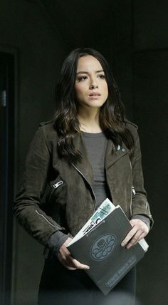 a woman holding a book in her hands and looking off to the side while standing