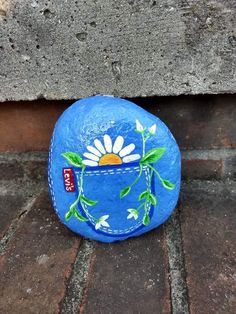 a painted rock sitting on the ground next to a brick wall with a flower in it