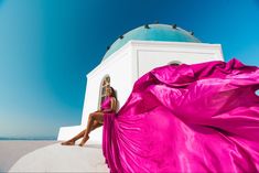 a woman in a pink dress sitting on the edge of a white building with a blue dome