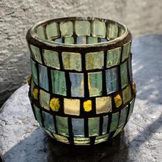 a glass vase sitting on top of a stone table next to a gray brick wall