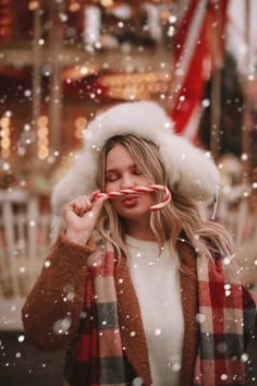 a woman holding a candy cane in front of her face while wearing a santa hat