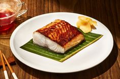 a white plate topped with fish next to a cup of tea and chopsticks