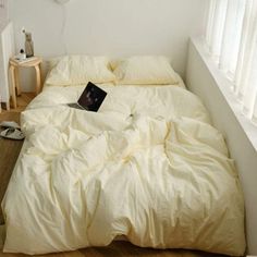 an unmade bed with a laptop on it in a bedroom next to a window