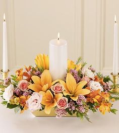 an arrangement of flowers and candles is displayed on a table with white walls in the background