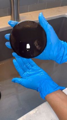 a person wearing blue gloves holding a black object in front of a sink with soap on it