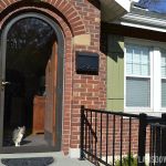 a cat is sitting in the doorway of a brick house with black iron railings