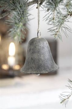 an old bell hanging from a pine tree with candles in the back ground behind it