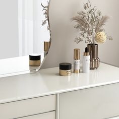 a white dresser topped with lots of bottles and vases next to a large mirror