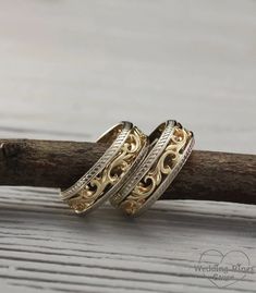 two gold rings sitting on top of a piece of wood next to a tree branch