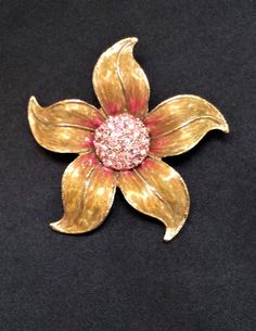 "This is a vintage pre-owned flower brooch.  This pretty flower has gold enamel petals with pink enamel details that highlight the sparkling pink center rhinestones. Each petal is detailed with a fine glittering gold tone outline. The brooch measures 2.5\" in diameter and has a secure rollover clasp. The brooch is in wonderful condition and will look fabulous on a jacket or little black dress. Thank you for looking!  Please remember this is a vintage item and as with all vintage jewelry, there w Pink Flower Enamel Brooch, Gold Flower-shaped Brooch With Floral Decoration, Pink Flower Enamel Pin, Vintage Pink Enamel Brooch Pin, Vintage Pink Enamel Pin Brooch, Collectible Gold Flower Enamel Pin, Vintage Pink Collectible Brooches, Vintage Pink Enamel Brooches, Pink Details