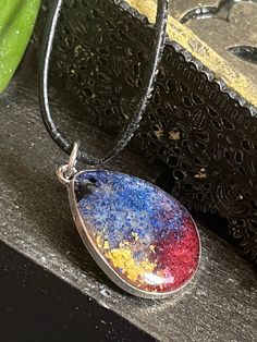 This necklace was handcrafted using resin, alcohol inks, and mica powders. Brilliant shades of blue, red and gold are framed by the silver of the bezel and the chain is made of 925 sterling silver. Hand Painted Adjustable Teardrop Jewelry, Multicolor Teardrop Spiritual Jewelry, Handmade Resin Teardrop Jewelry, Multicolor Teardrop Necklace For Gift, Adjustable Resin Teardrop Jewelry, Silver Hand-painted Resin Necklace, Silver Hand Painted Resin Necklace, Hand Painted Silver Resin Necklace, Multicolor Teardrop Drop Necklace For Gift