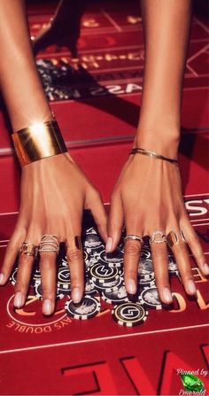 two hands with gold rings on top of a red carpet and playing roulee