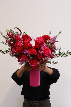 a person holding a pink vase with red flowers on top of it and covering their face