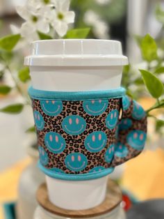 a coffee cup sleeve is sitting on top of a wooden stand with flowers in the background