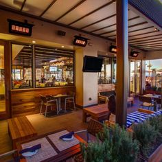 an outdoor patio area with tables and chairs, televisions on the wall and large windows