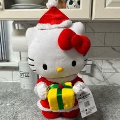 a hello kitty stuffed animal with a gift wrapped around it's neck and wearing a santa hat