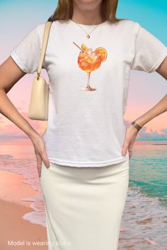 Cruise the Italian riviera in our y2k baby tee shirt with a trendy large Aperol Spritz graphic  - the perfect European summer aesthetic. This 90s baby tee shirt makes a preppy Pinterest summer outfit and better yet get a matching gift for your bestie in crime - make sure the bartender keeps the drinks coming! This minimal print top is perfect to style with your low rise jeans or skirt and y2k sunglasses for the perfect retro 2000s clothing fit. Get yours now and join the Aperol Spritz cocktail club, Cin Cin! 🍹 ------------------------------------------------------------------------------------------------------   Size guide Please take a moment to see the size chart, both in inches and cm, and measure against your favorite tee to make sure you get the best fit for you. This is a unisex st Retro Summer T-shirt With Front Print, Fitted Graphic Print T-shirt For Summer, Y2k Summer Tops With Screen Print, Y2k Style Summer Tops With Screen Print, Y2k Style Screen Print Tops For Summer, Y2k Style Screen Print Summer Tops, Y2k Summer Screen Print Tops, Y2k Printed Short Sleeve Tops, Y2k Style Printed Tops For Summer