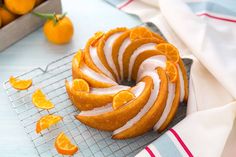 an orange bundt cake with white icing and sliced oranges in the background