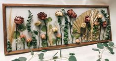 an arrangement of flowers and leaves on display in a wooden frame with gold leaf accents