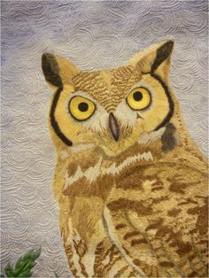 an owl with yellow eyes sitting on top of a quilted tablecloth covered surface