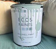 a white paint can sitting on top of a bed next to two pillows and a pillow