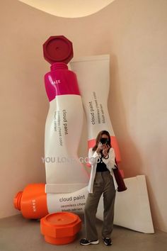 a woman taking a photo in front of two large white and pink bottles on display