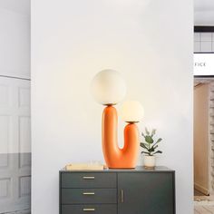 an orange vase sitting on top of a dresser next to a lamp and potted plant