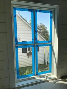 an open window with blue tape on the side of it and a white house in the background