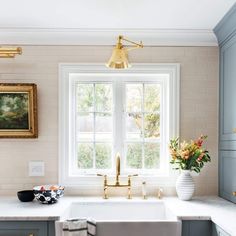 a white kitchen sink sitting under a window next to a vase with flowers in it