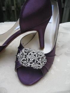 a pair of purple high heeled shoes with a crystal brooch on the side