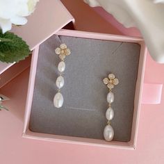 a pair of pearl and diamond earrings in a pink box with flowers on the side