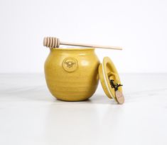 a yellow ceramic jar with a wooden honey dipper and lid sitting on a white surface