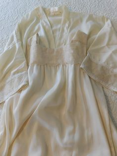 This is a gorgeous custom made vintage Peignoir nightgown set.  This set was made in the 1970's as a wedding night nightgown and robe.  This set is in excellent condition with no tears or stains.  The color is a soft ivory or off white.  I have photographed this set against both wood and white to show the color more accurately.  This set is made of a soft satin fabric (that does not snag) but I am not sure of the type of fabric.  The bottom hemline of this robe is trimmed in a very wide 6" floral French lace and has two nice deep pockets on the front.   Robe has a very nice long tie and is very nice and full.   The lace is gorgeous!  I have hand washed this set and pressed it so it is clean and free of any odors or stains. Even though there is not size label, I would size this peignoir set Vintage Peignoir, Night Gown Lingerie, Nightgown And Robe, Nightgown Robe, Wood And White, Nightgown Sets, Peignoir Sets, Lingerie Sets, Wedding Night