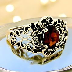 Step into a world of timeless elegance with our Vintage Natural Garnet Solitaire Filigree Ring. Crafted with exquisite attention to detail, this stunning piece showcases a 7x5 mm oval faceted natural garnet stone, radiating rich hues that capture both light and attention. The ring's top measures a generous 12.5 mm, nearly 1/2 inch in length, making it a striking statement piece for any occasion. Beautifully stamped with "925," this ring is made from solid sterling silver, ensuring both durability and a lasting shine that will enhance the allure of your jewelry collection. Every element of this garnet solitaire ring reflects artisanal craftsmanship, featuring a delicate filigree design that adds a touch of vintage charm. The intricate detailing of the ring enhances its timeless beauty, maki Ring Elegant, Garnet Stone, Filigree Design, Everyday Accessories, Filigree Ring, Timeless Treasures, Solitaire Ring, Vintage Charms, Timeless Beauty