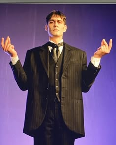 a man in a suit and tie holding his hands up while standing on a stage