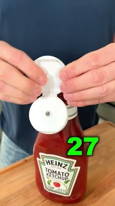 a person is holding a jar of ketchup on a cutting board with the lid open