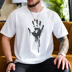 Stand out with this unique unisex gothic handprint shirt, featuring a bold black ink dripping handprint design. Perfect for Halloween or any occasion, this spooky graphic tee combines grunge style with casual comfort. Made from high-quality materials, this shirt is soft and durable, ideal for everyday wear. Whether you're into gothic fashion or just looking for a standout piece, this handprint shirt is a perfect addition to your wardrobe. Available in various sizes, it's a great gift for horror White Graffiti Print Tops For Halloween, Black Crew Neck T-shirt With Paint Splatter, White Gothic T-shirt For Streetwear, Black Graphic Tee With Paint Splatter, Grunge Halloween T-shirt With Graffiti Print, Grunge T-shirt With Graffiti Print For Halloween, Grunge Graffiti Print T-shirt For Halloween, Black Halloween Graffiti Print T-shirt, Black Halloween T-shirt With Graffiti Print