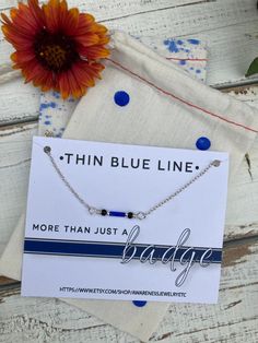 the thin blue line necklace is on display next to a flower and an envelope that says, more than just a badge