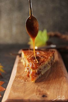 a wooden cutting board topped with a slice of pie covered in caramel and syrup