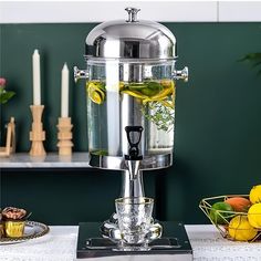 a table topped with a silver vase filled with liquid and lemons on top of it