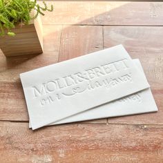 two white placemats sitting on top of a wooden table next to a potted plant