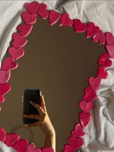 a person taking a photo of a heart shaped mirror with their cell phone in it