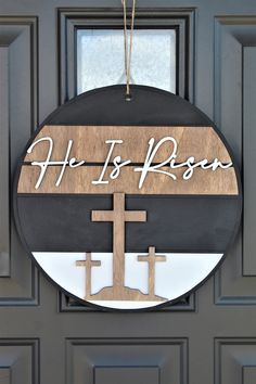 a wooden sign that says he is risen hanging on a door with a cross in front of it