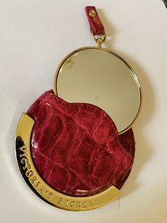 a red purse with a mirror hanging from it's side on a white surface